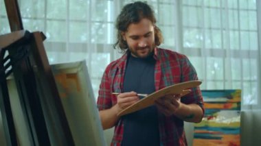 Bir ressam, büyük sanat paletini birçok renk ve resimle tutarken neşeyle gülümserken çok mutlu görünür. 4k