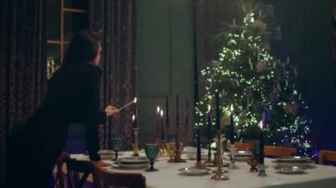Siyah elbiseli çok güzel bir kadın yemekten önce Noel masasını dekore etti. Mumları çok şehvetli ve harika bir Noel atmosferi ile yaktı..