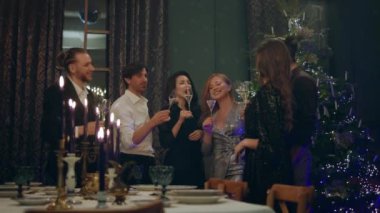 Oturma odasında muhteşem bir dekor grubu olan yetişkinler çok karizmatik ve güzel bir şekilde Noel 'i birlikte kutluyorlar Noel ağacının yanında duruyorlar ve şampanya içiyorlar. 4k