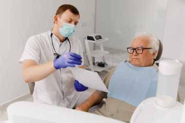 At the dentist check up old man sitting on the dentist chair the doctor explains to the patient the process of work.