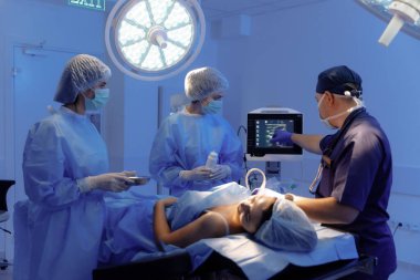 A male and woman surgeon are working together to prepare a patient for surgery in a hospital room.