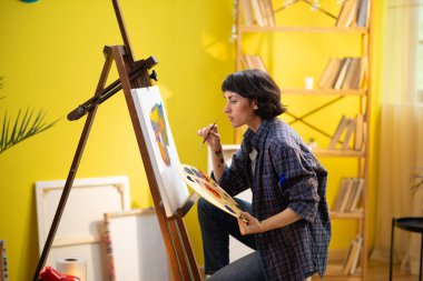 Güzel bir ressam kadın, zaten parlak olan sanat eserine küçük detaylar ekliyor ve sanat stüdyosundayken daha da iyi görünmesi için üzerinde çalışıyor. Portre