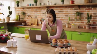 Mutfak adasındaki mutlu ev hanımı Happy, internetten sipariş vermek için meyve suyunu içer ve bilgisayarına bakar. Mutfakta çok heyecanlı vakit geçirir. 4k