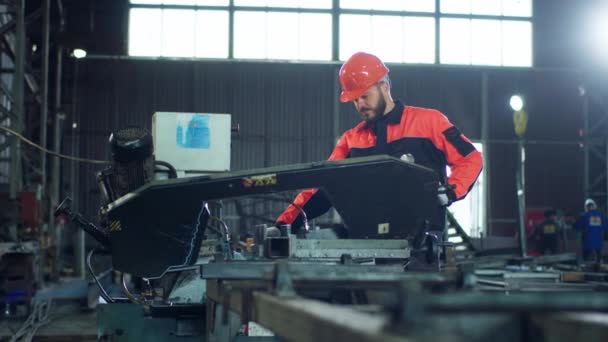 カメラの前に安全装置を身に着けている重い機械類の上に働く産業地帯のカリスマ的な男の工場労働者 — ストック動画