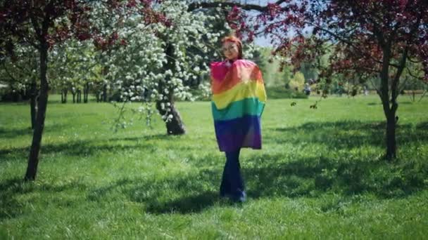 完美的阳光灿烂的一天 站在公园中央的草地上 高举着彩虹Lgbt旗 对着摄像机摆姿势 — 图库视频影像