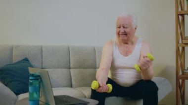 Yaşlı adam evde otururken ve dizüstü bilgisayarda bir şeyler izlerken iyi bir ruh hali içinde ağırlık kaldırıyor ve pazıları eğitiyor. 4k
