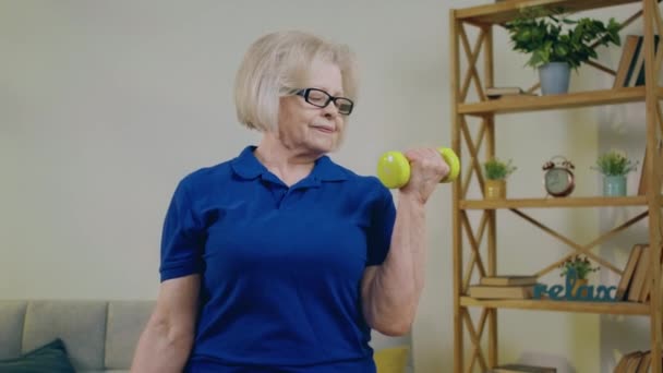 カメラの前に美しい老婆が自宅でトレーニングを行い 重量を持ち上げて二頭痛をトレーニングします 4Kについて — ストック動画