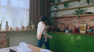 Modern ve tasarlanmış mutfak kısa saçlı güzel bir kadın mutfak adasına yürürken su ısıtıcısını tutuyor ve elektrikli ocağı yakıyor. 4k