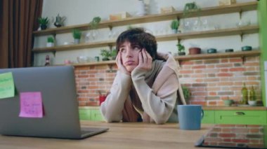 Geniş ve büyük mutfak. Mutfak adasında dizüstü bilgisayarın önünde duran yorgun ve kötü hisseden kadın çaydanlığın kaynamasını bekliyor. 4k