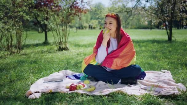 非常に幸せで笑顔の女性レズビアンは リンゴを食べてLgbt旗を保持している公園の真ん中に自分自身とピクニック時間を持っています 4Kについて — ストック動画