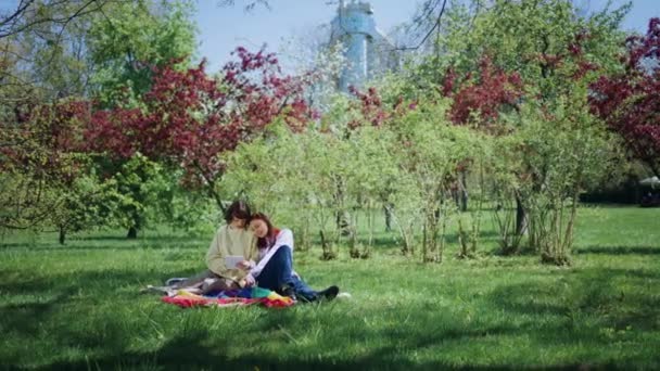 晴れた日 レズビアンカップルは非常にカリスマ的で草の上に横たわり Lgbtライフスタイルのデジタルタブレットコンセプトを見ています 4Kについて — ストック動画