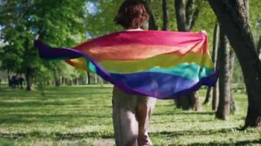 Parkta koşan kısa saçlı güzel bayan mükemmel güneşli bir günde arkasında lgbt bayrağını tutuyor..