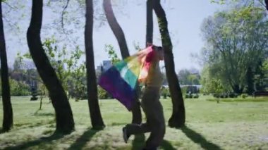Kısa saçlı mutlu lezbiyen kadın lgbt bayrağını al ve parkta koştuğu zamanın tadını çıkar..