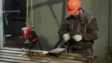 Metal fabrikasında çalışan profesyonel demirci metali ölçüyor ve güvenlik ekipmanı ve kask takıyor..