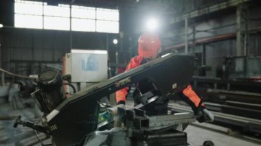 Güvenlik teçhizatı ve miğferi olan iyi görünümlü bir fabrika işçisi ağır endüstriyel makineleri kullanarak metali kesiyor..