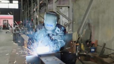 Metal fabrikasındaki profesyonel kaynakçı metal parçayı alıyor ve güvenlik ekipmanı ve kask takıyor. 4k