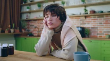 Kameraya yakın çekim. Üzgün ve yorgun kadın hastalanıyor. Mutfak adasında dikiliyor ve sıcak bir içecek hazırlıyor. 4k