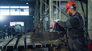 Metalle çalışan demirciye yakın çekim yapan imalatta çekilen videoda diğer fabrika çalışanları arka planda..
