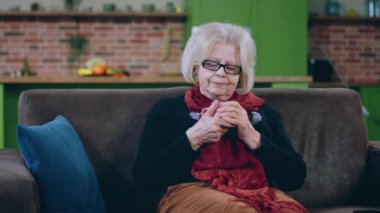 Kameranın önünde yaşlı, çok karizmatik bir kadın koltukta oturmuş elinde sıcak bir içecek tutarak etrafa bakıyor ve düşünen bir yüzü var. 4k