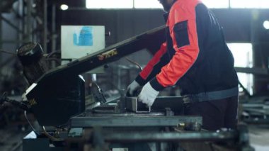 Endüstriyel bölgedeki yakışıklı genç fabrika işçisi kask ve eldiven taktığı ağır endüstriyel makineleri kullanarak metali kesmeye hazırlanıyordu. 4k