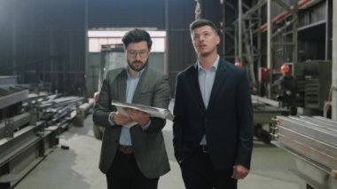 Kameranın önünde iyi görünümlü iki Kafkas erkek ana mühendis ve yatırımcı yeni proje planını elinde tutan imalat fabrikası mühendisi ile yürüyorlar ve yatırımcıya
