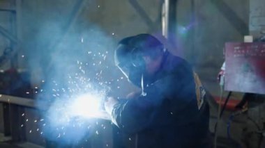 Metal fabrikasındaki kameranın önünde kaynak yapan adam metali elektrot kullanarak kaynaklıyor. 4k