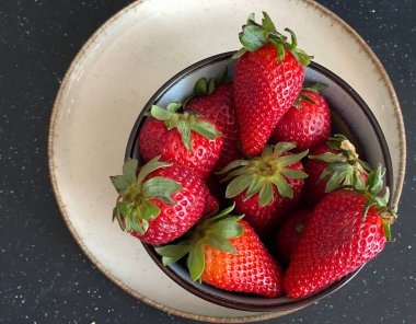 Siyah arka planda bir kasede taze çilek.