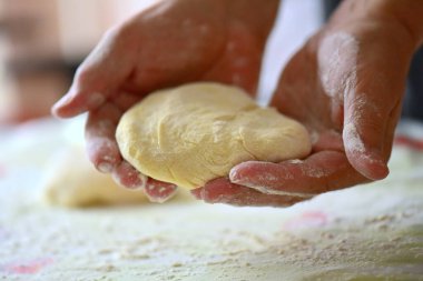 Masasında un olan hamuru yoğuran bir kadının elleri.
