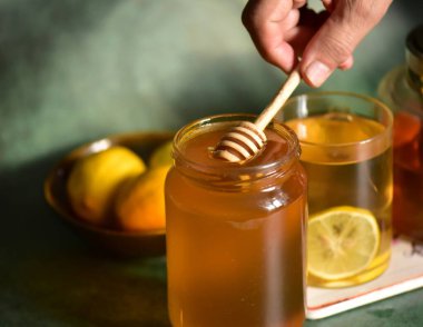 Bir kadının eli bal kavanozunun üzerinde tahta bir bal çubuğu tutuyor..