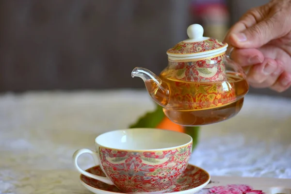 Enjoying drinking prepared tea. A man pours tea from a porcelain teapot into a beautiful colorful cup on a wooden table.