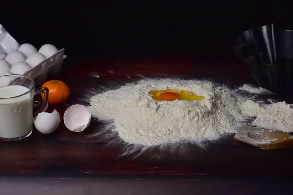 Koyu bir ahşap zemin üzerinde hamur, un, yumurta ve yumurta pişirme süreci.