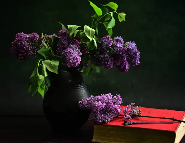 Beautiful lilac flowers in vase with book on black background