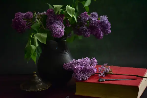 A closeup shot of a purple lilac flower with a book on a black background