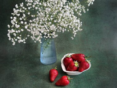 Çilekler, çiçekler ve nane şekeriyle dolu bir vazoda, ahşap bir arka planda.