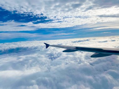 Mavi gökyüzünde bulutlarla uçan bir uçağın kanadı. Seyahat ve tatil kavramı.