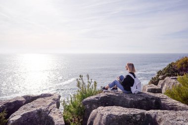 Turizm konsepti. Sırt çantalı genç bir kadın okyanus manzarasının keyfini çıkarıyor..