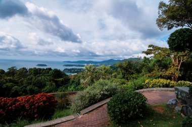 Phuket tropik plaj manzaralı. Okyanus kıyıları, yeşil tepeler, bulutlu gökyüzü olan güzel bir manzara. Phuket, Tayland.