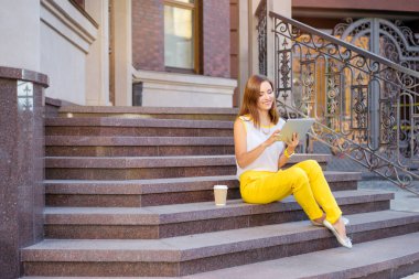 Kahve molası. Merdivenlerde otururken tablet bilgisayar kullanan genç ve güzel kadın.