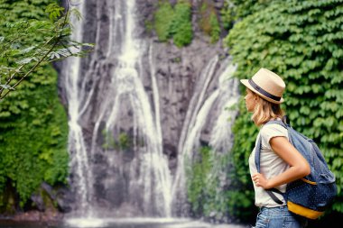 Tropikal seyahat. Genç kadın şelale manzarayı sırt çantası ile şapkalı.