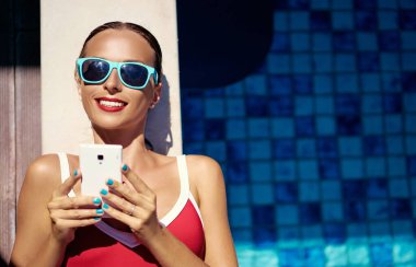 Tatil ve teknoloji. Yüzme havuzunda akıllı telefon kullanan güzel bir kadının renkli portresi..