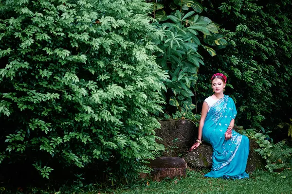 美丽的年轻的高加索女人 穿着传统的印度服装 有新娘的妆容和珠宝 宝莱坞舞蹈演员在萨里和亨纳手拉手在绿色的花园上散步 — 图库照片