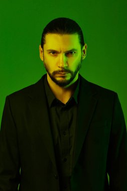 Yeşil arka planda takım elbise giyen sakallı adamın stüdyo portresi..