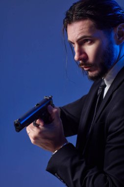 Gizli ajan ya da casus gibi giyinmiş, silahlı sakallı bir gencin stüdyo portresi..