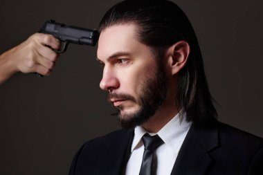 John Wick 'e benziyor. Gizli ajan ya da casus gibi giyinmiş, silahlı sakallı bir gencin stüdyo portresi..