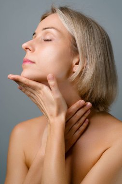 Cilt bakımı. Güzel yüz masajlı sarışın kadın. Makyaj yok. Gri arkaplan.