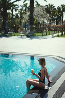 Tatil keyfi. Genç ve güzel kadın yüzme havuzunda kokteyl içme.