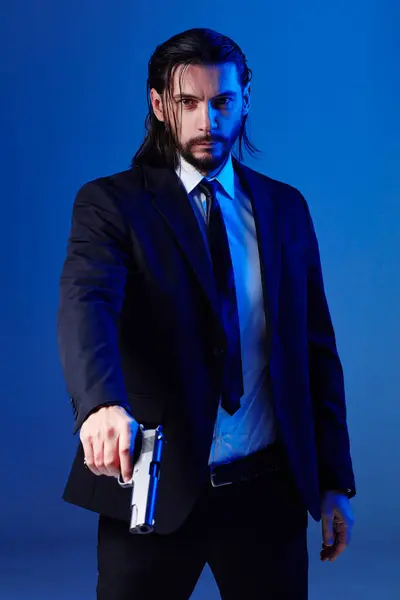 Looking like movie hero. Studio portrait of bearded young man with gun, dressed as a spy or secret agent.