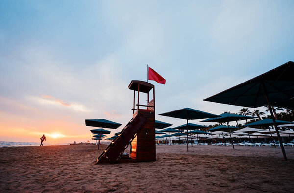 Red riscue flag on lifeguard tower on sea beach at sunset time.