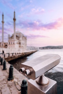 İstanbul 'da sahil kenarındaki gezinti alanının yanındaki madeni para işleten dürbün izleyicisi körfeze ve kente bakıyor.