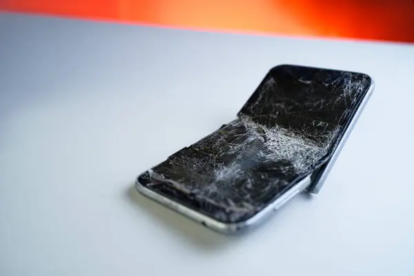 Mobile smartphone with broken screen on white table.